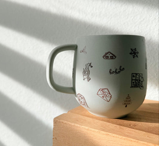 White mug with black and red designs on a wooden surface with sunlight casting shadows.