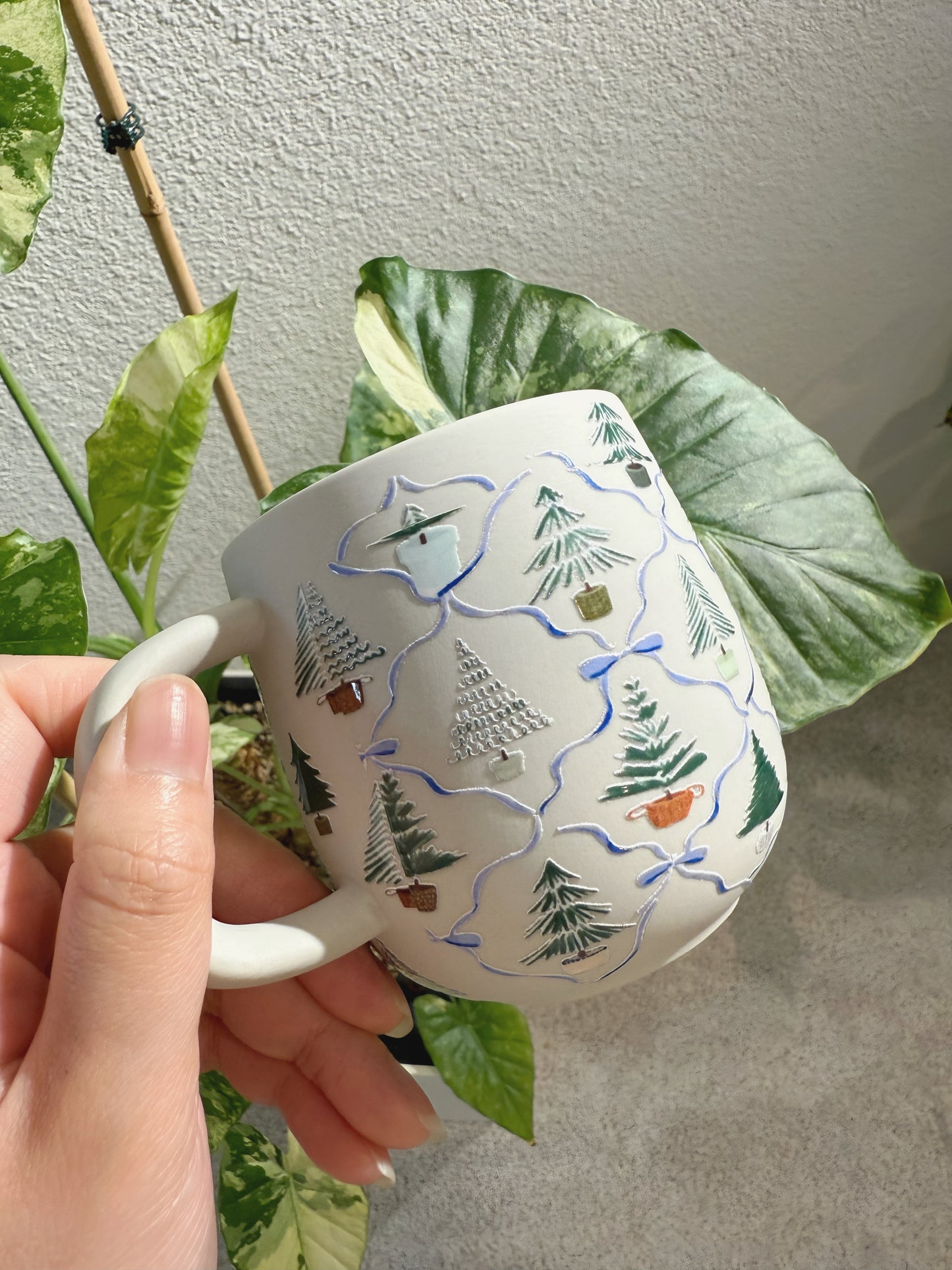 Hand holding a mug with nature-themed design against a leafy background