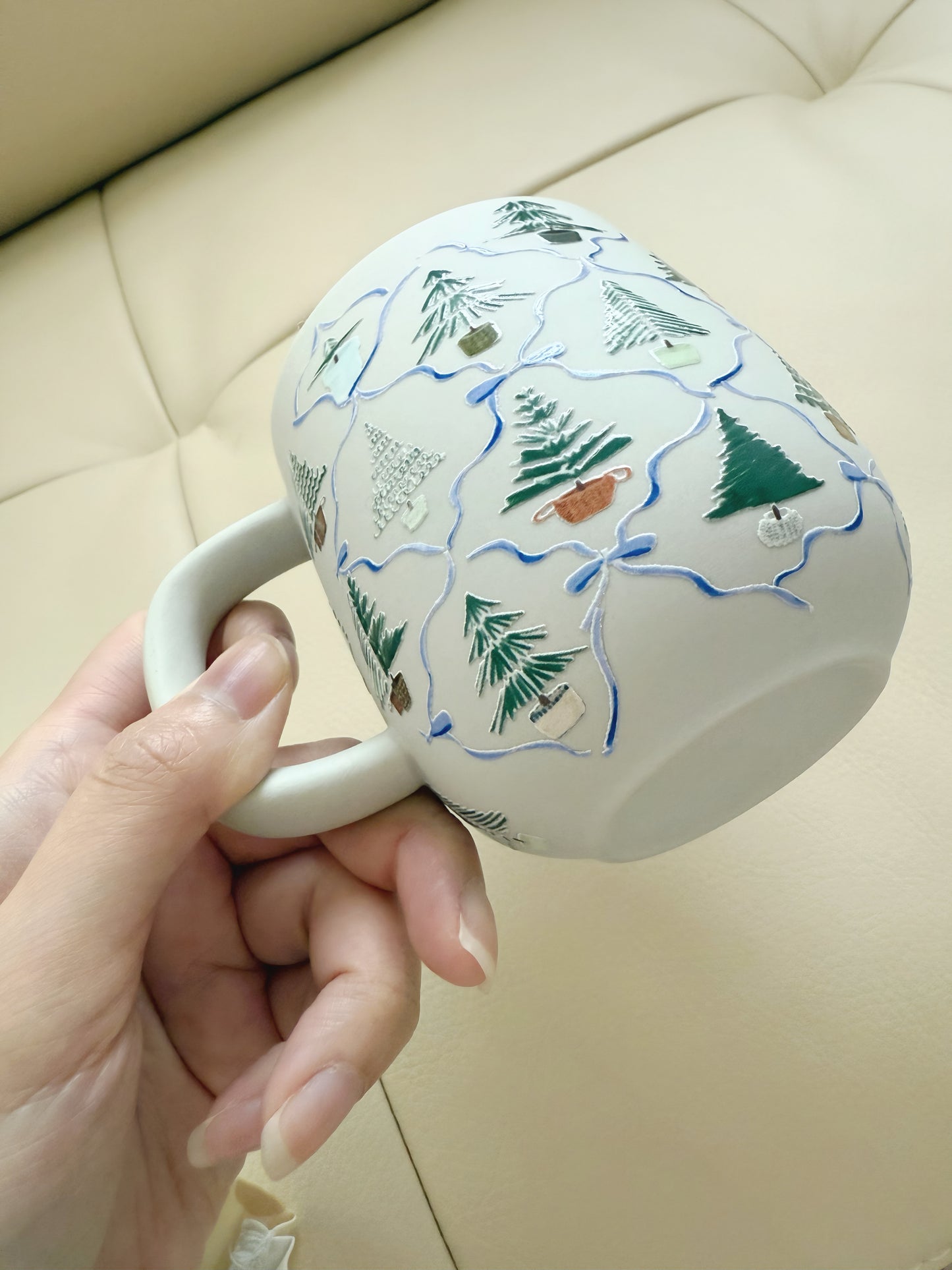 Hand holding a mug with nature-themed design on a beige surface